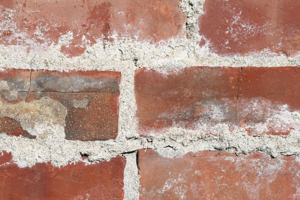 Close-up of a weathered red brick wall with white mortar and peeling white paint