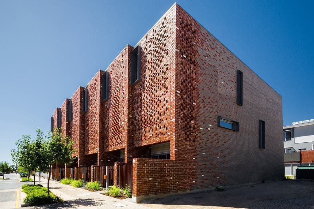 Modern brick building with perforated facade along a sidewalk on a sunny day