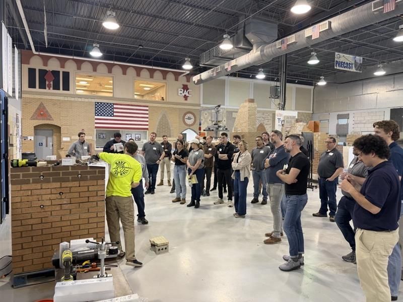 People gathered at the International Masonry Institute, standing and watching an event near a brick structure and U.S. flag.