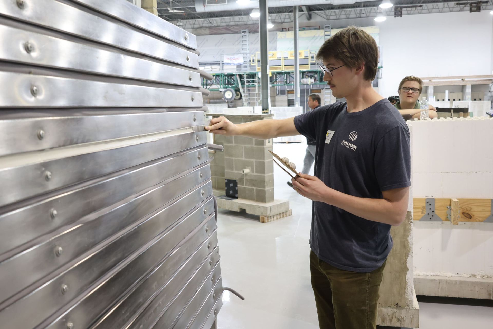 Person testing sealant repair on a large metallic panel in an industrial workshop.