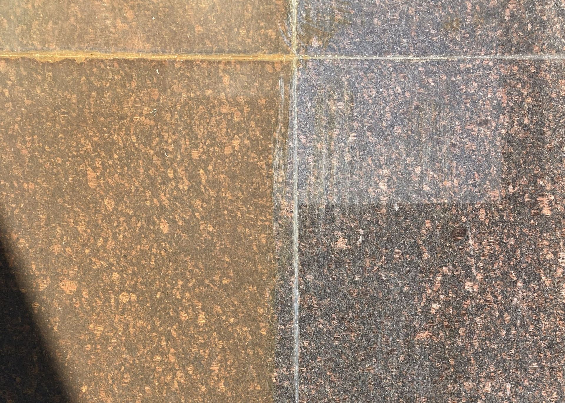 Close-up of a weathered stone surface with tan, gray, and speckled brown sections divided by grout lines
