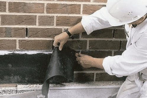Worker applying black waterproof membrane to the base of a brick wall