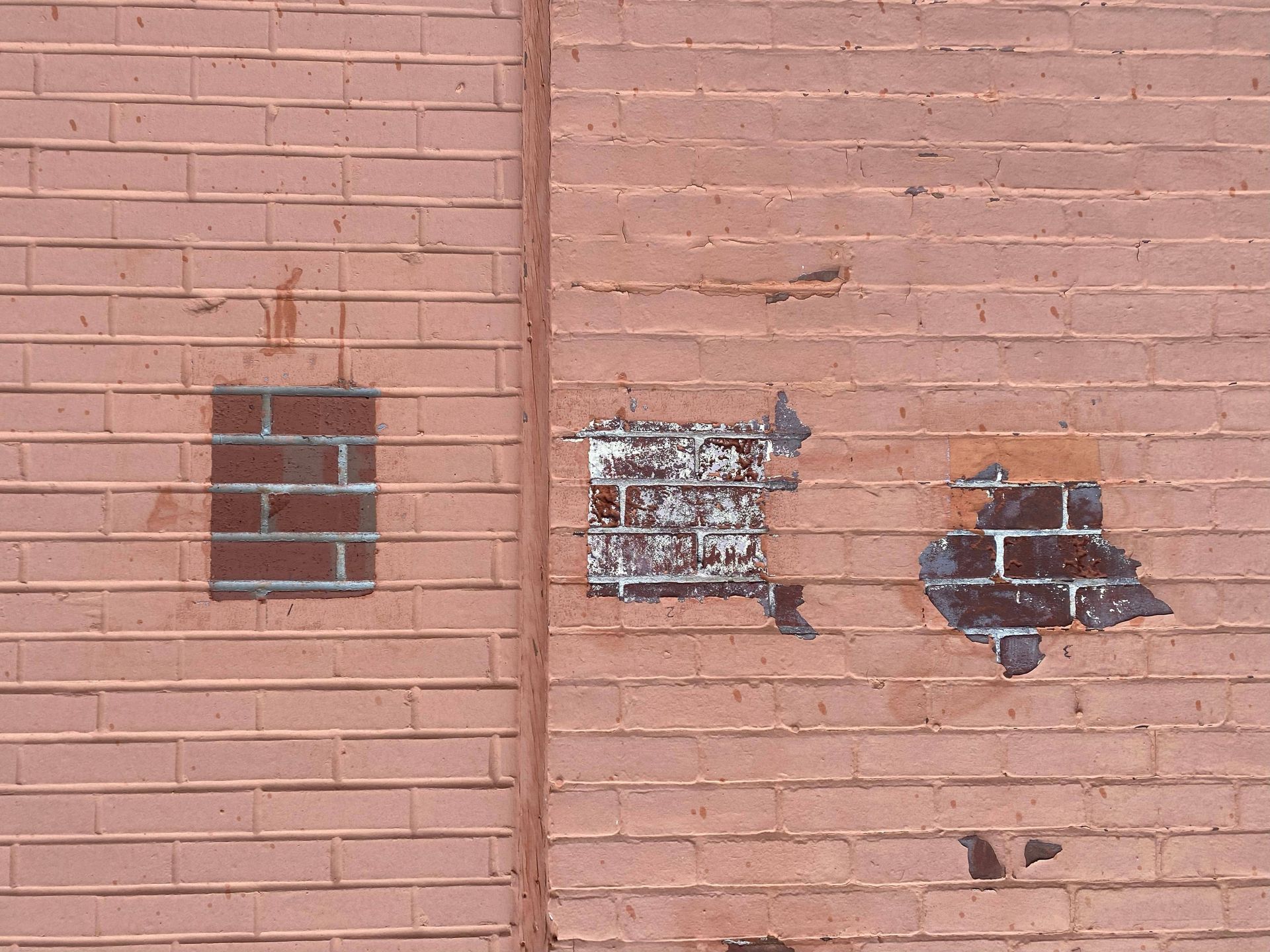 Pink brick wall with three small damaged or patched openings