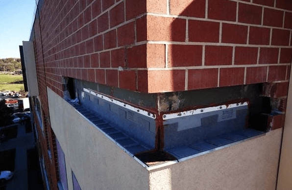 Damaged rooftop corner with red brick and peeling metal flashing above a white wall