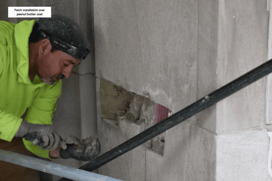 Worker in neon green shirt repairing a wall with a trowel beside a black pipe