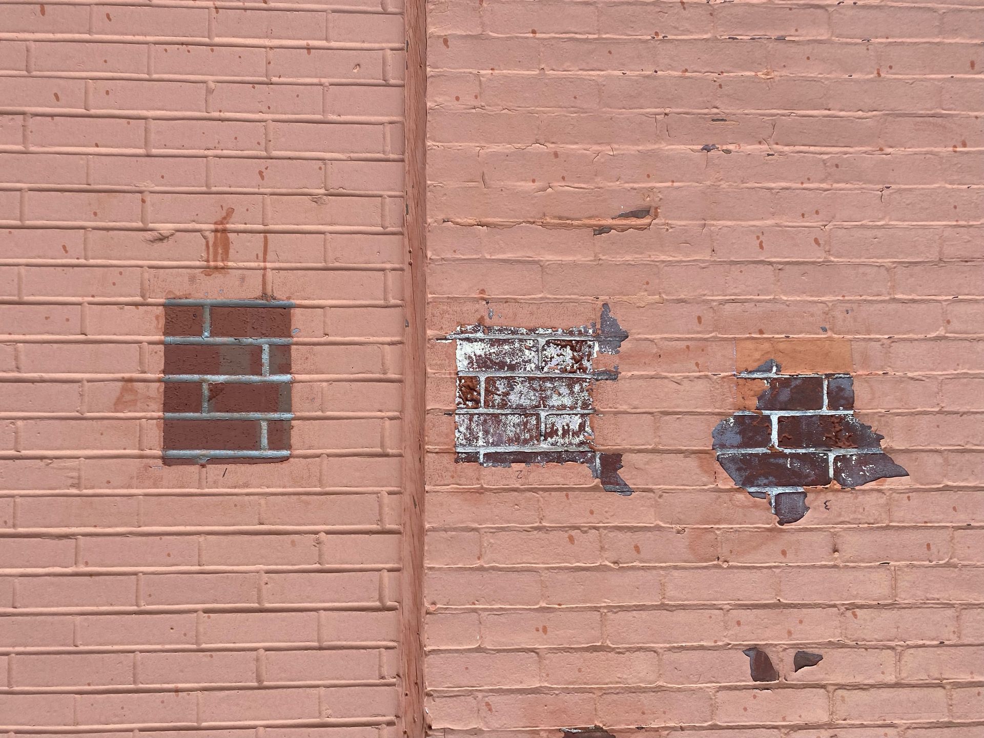 A pink brick wall featuring three rectangular patches of darker, differently textured bricks in varying states of repair.