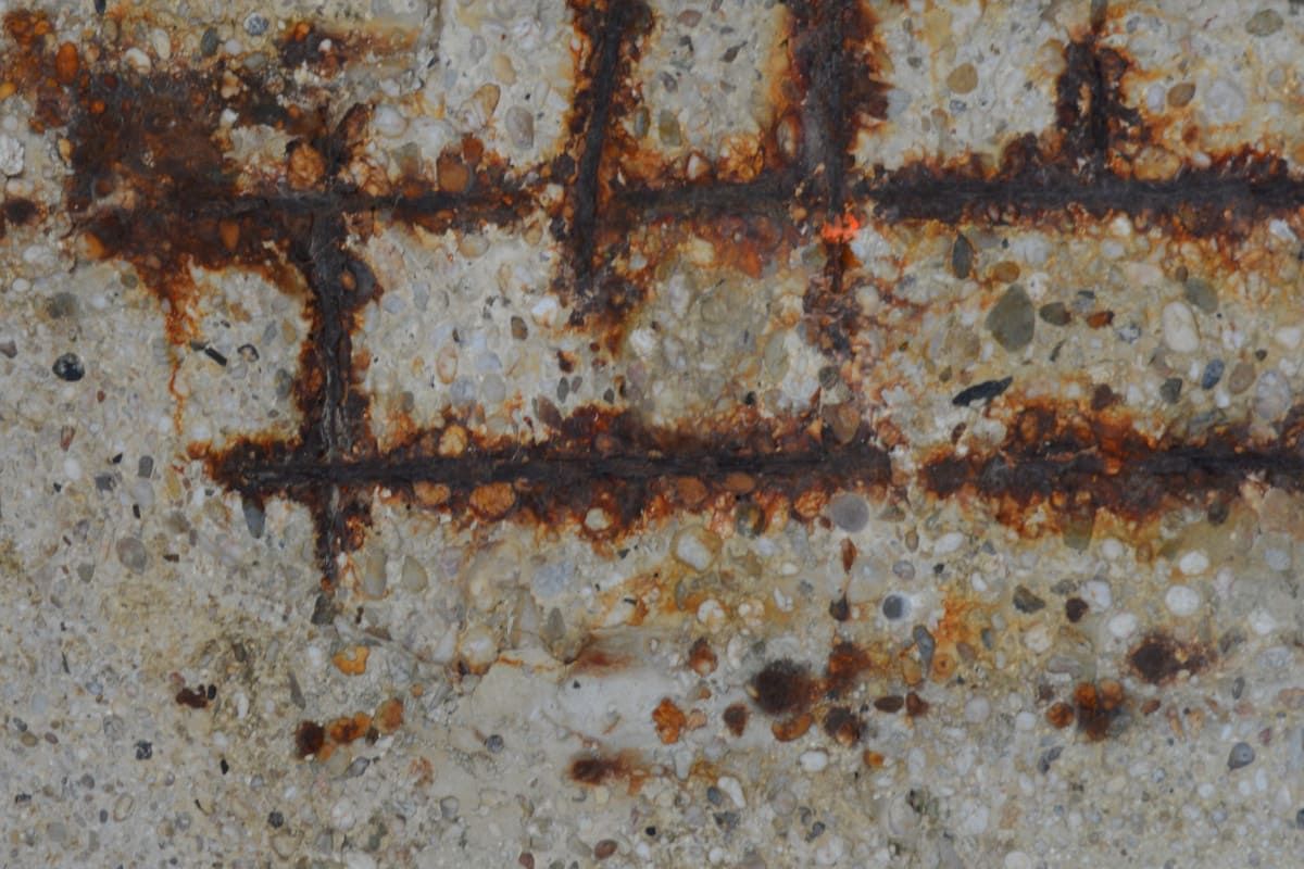 Close-up of a weathered concrete wall with rusty brown cracks and stains