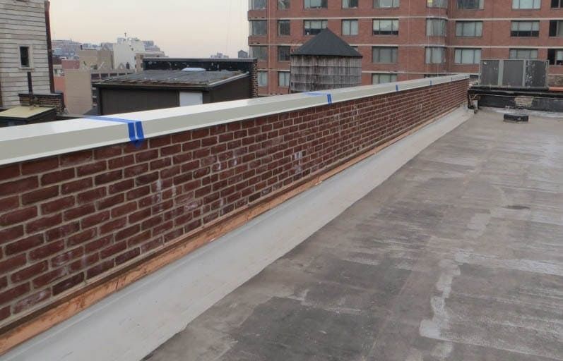Rooftop with a brick parapet wall and flat gray roofing, overlooking nearby buildings