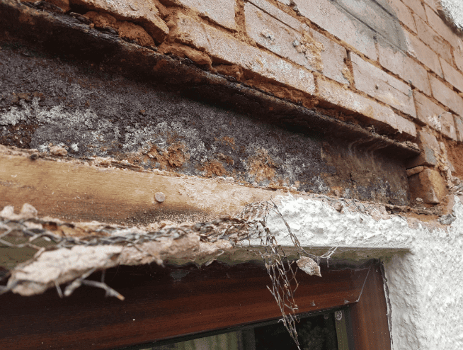 A close-up view of a severely rusted steel lintel above a window frame, with crumbling mortar and exposed brickwork.