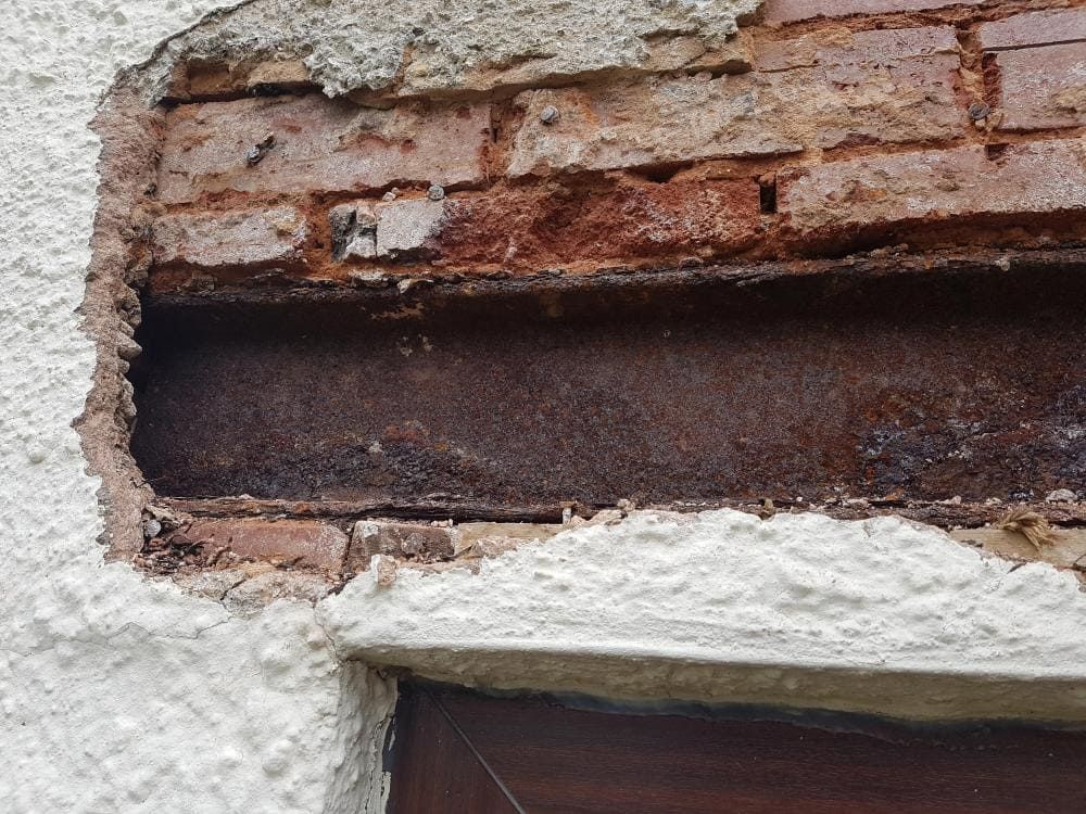 Close-up of a damaged plaster wall exposing a rusted brick cavity and dark gap beneath.