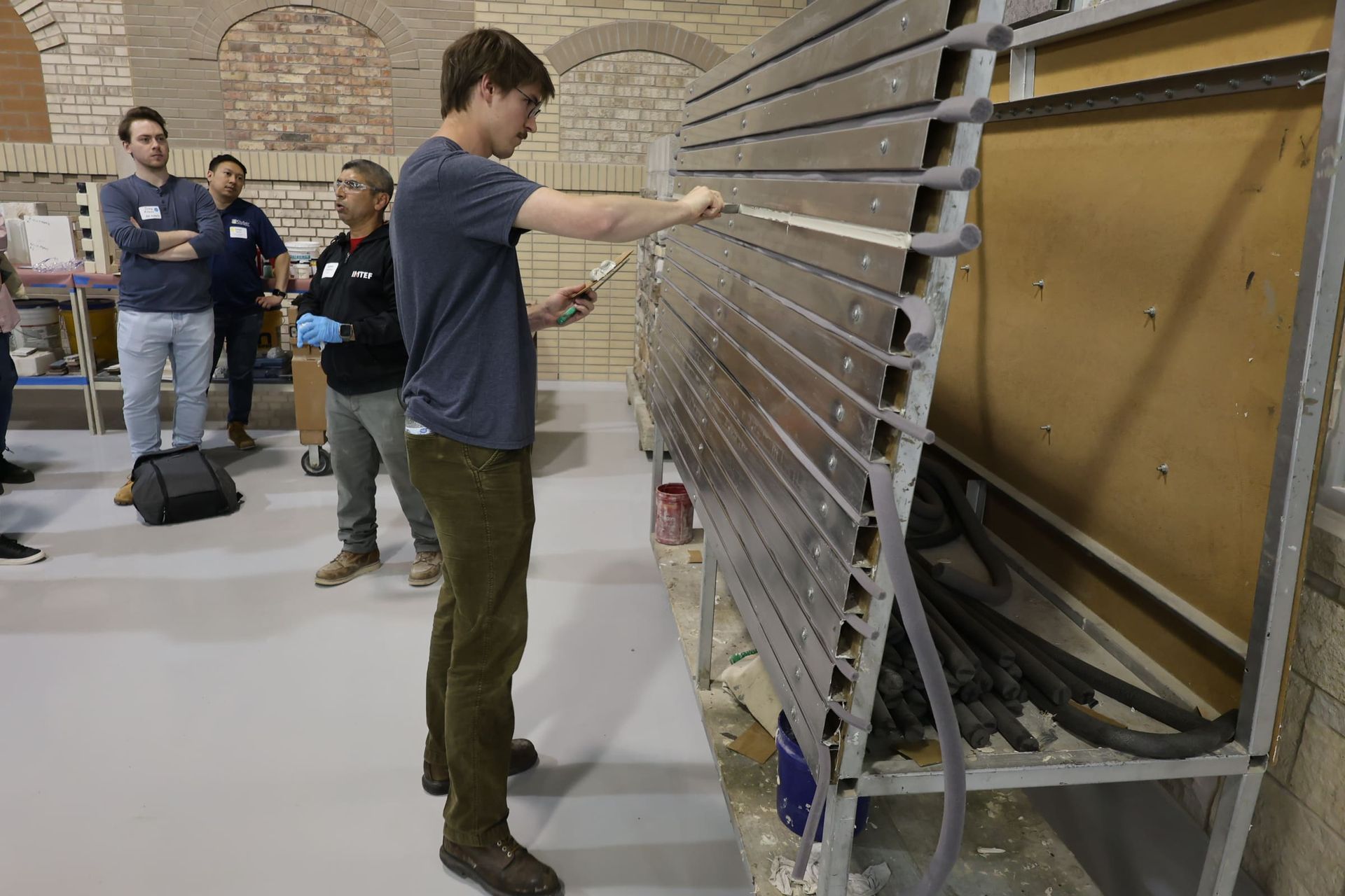 Person doing hands-on sealant installation at a workshop, with two people watching nearby.
