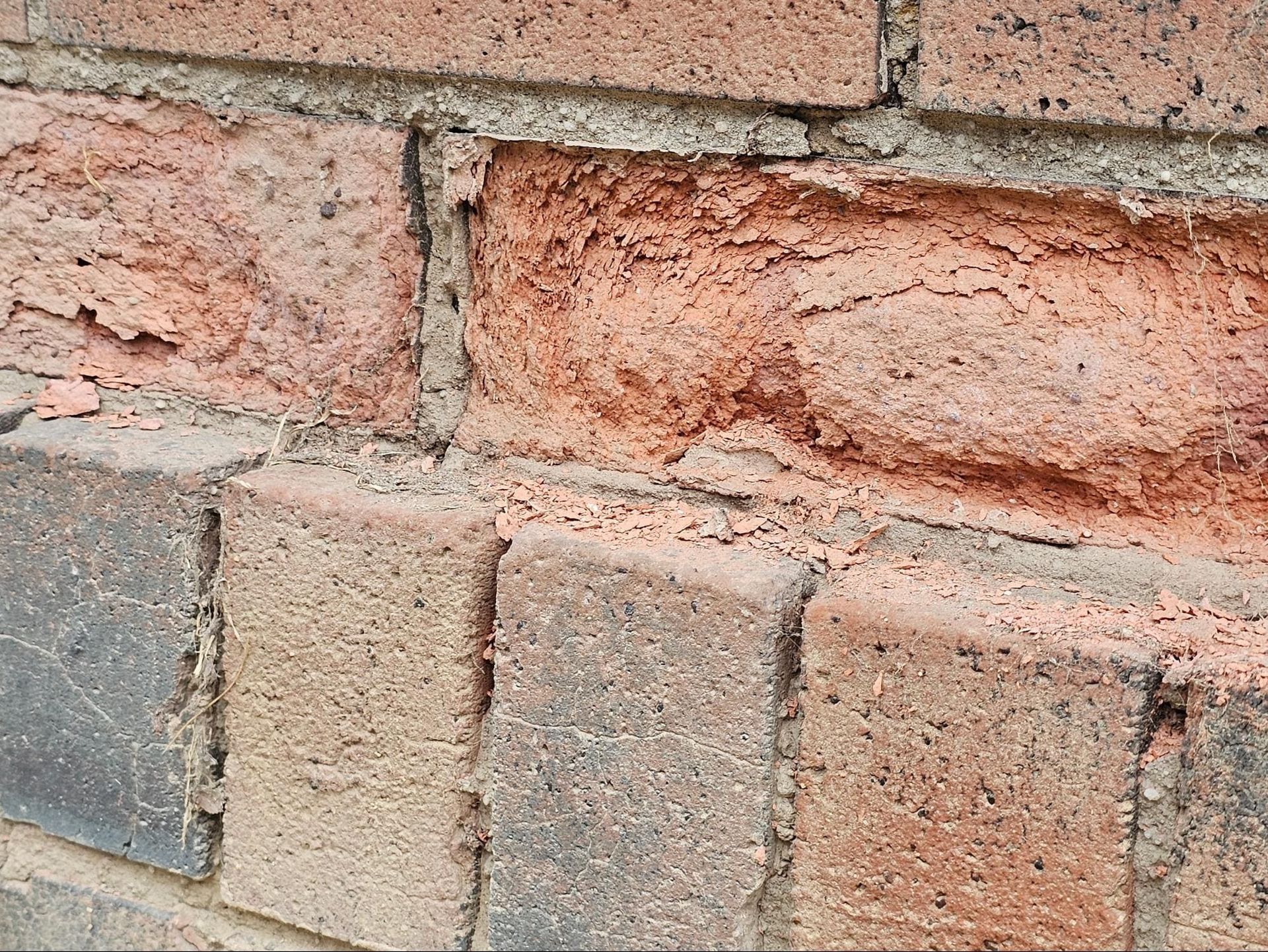 Close-up of a weathered red and tan brick wall with cracked mortar
