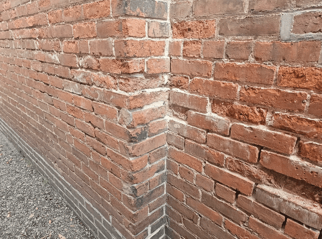 Close-up of a weathered red brick wall corner with a gravel path along the left side.
