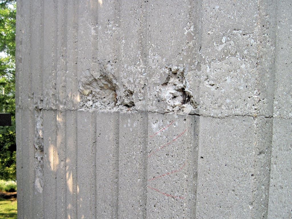 Cracked concrete wall with damaged patches and a vertical seam