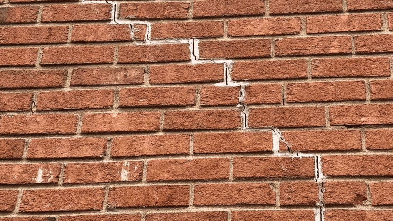 Red brick wall with a diagonal white crack running through the mortar lines