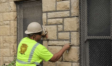Construction worker in neon vest and hard hat examining stone wall beside a window