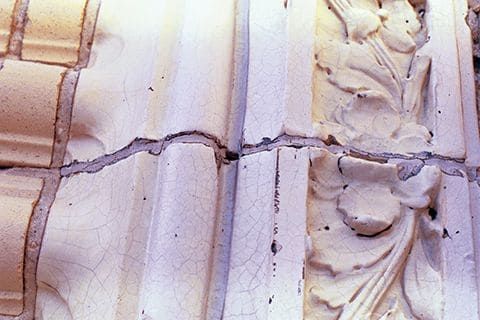 Close-up of a cracked, weathered stone wall with carved decorative details.