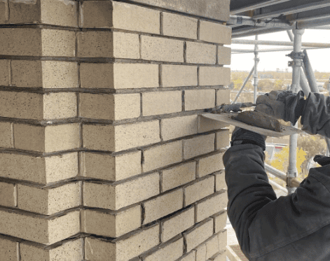 Worker tuckpointing a brick wall at a construction site under scaffolding