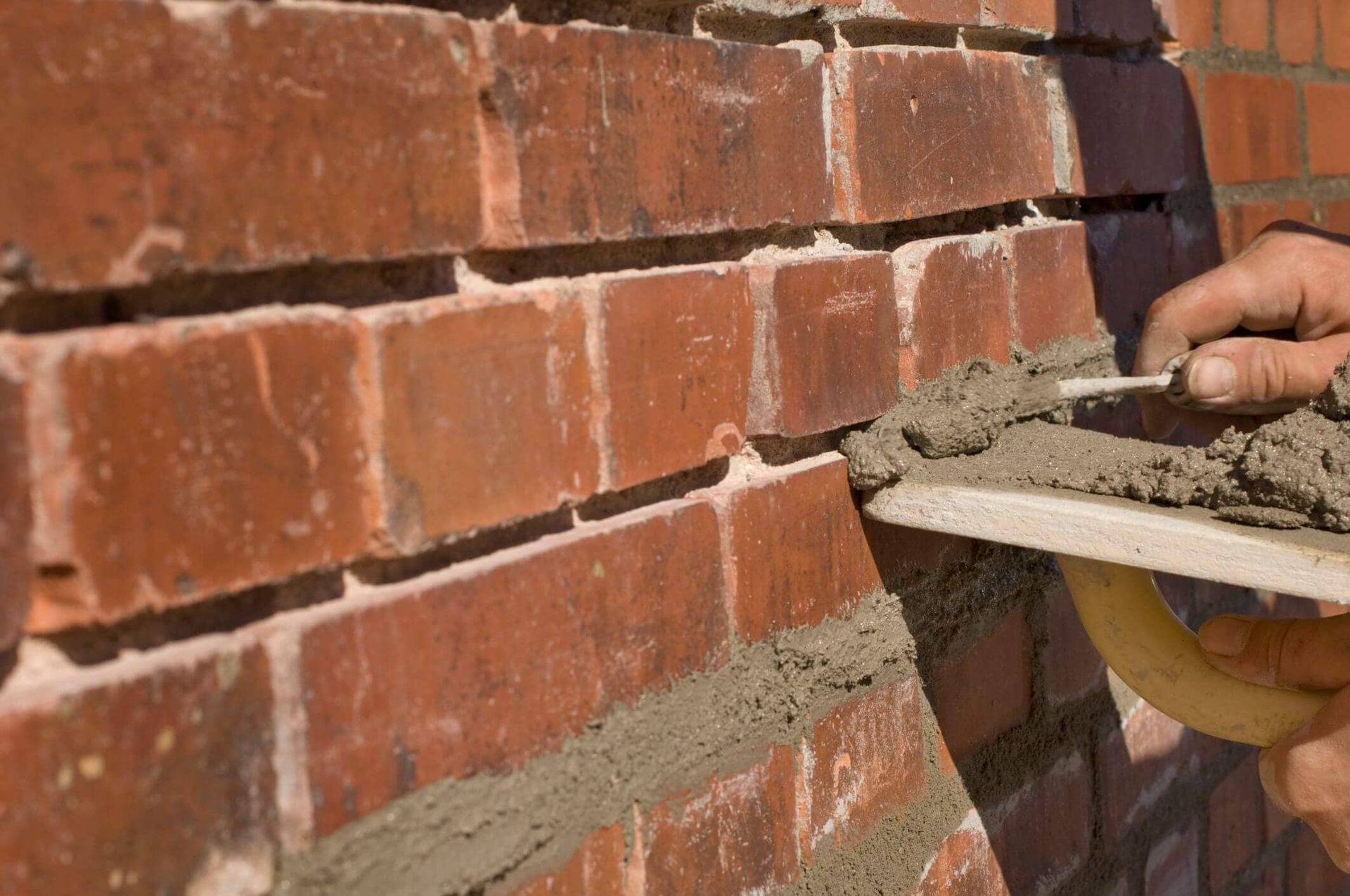 Hand applying mortar between red brick wall joints with a trowel