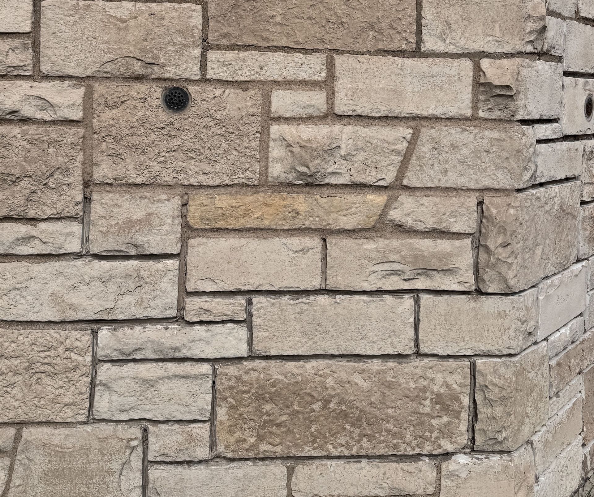 Beige stone wall corner with rectangular masonry blocks and a small black fixture