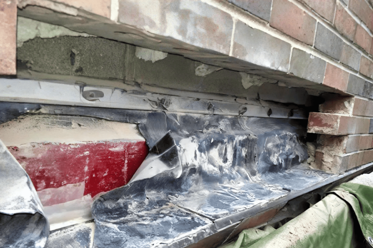 Damaged brick wall with exposed insulation and black waterproofing near a window opening