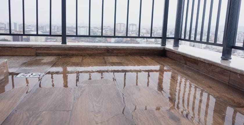 Wet wooden deck with puddles beside a black metal railing overlooking a snowy view