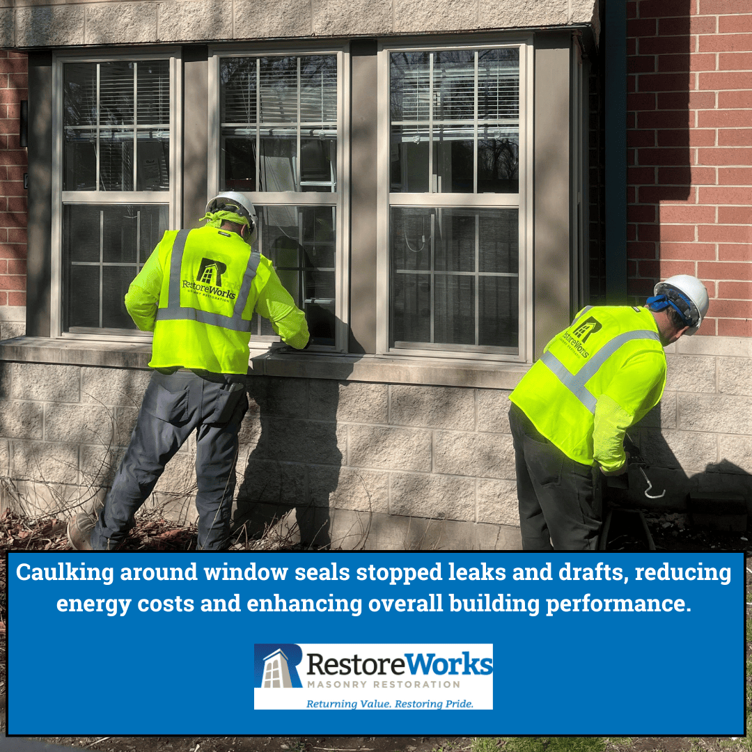 Two workers in neon yellow safety vests apply sealant to window frames on a brick building exterior.