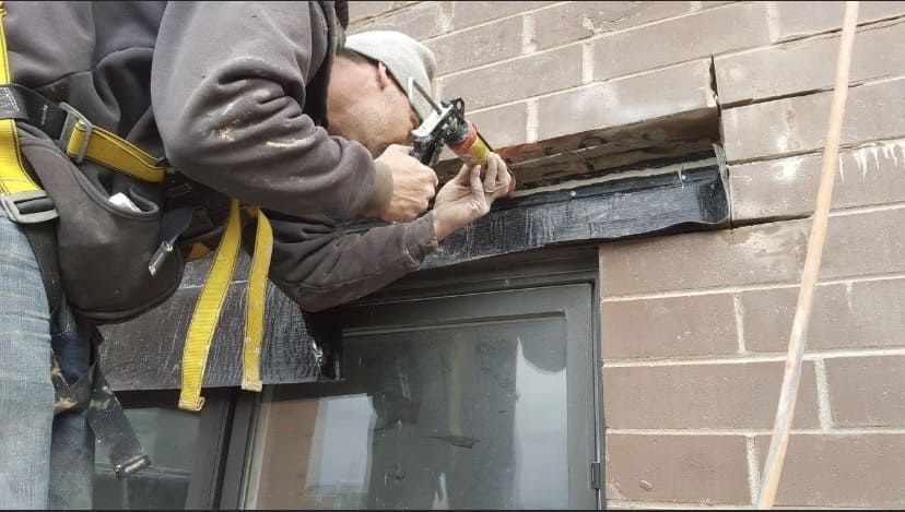 Worker using a power drill to install or repair trim above a window on a brick wall