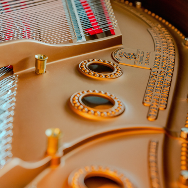 Close-up of a golden piano interior with strings, hammers, and ornate metal details