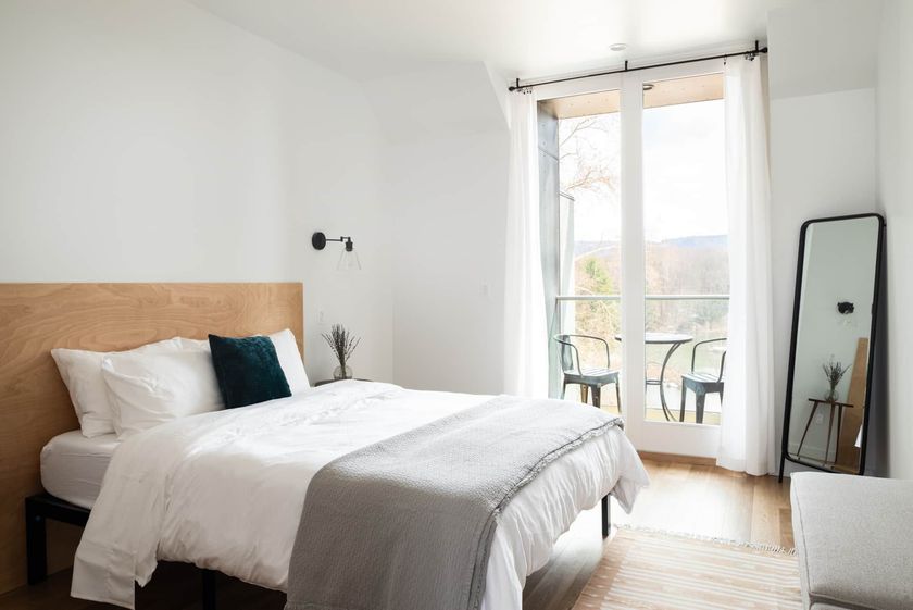 Bright bedroom with a bed, floor mirror, and open balcony doors letting in sunlight