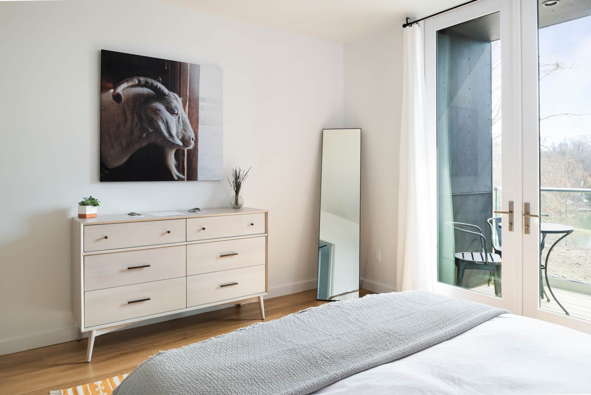 Bright bedroom with a white dresser, full-length mirror, bed, and large horse wall art near a balcony door