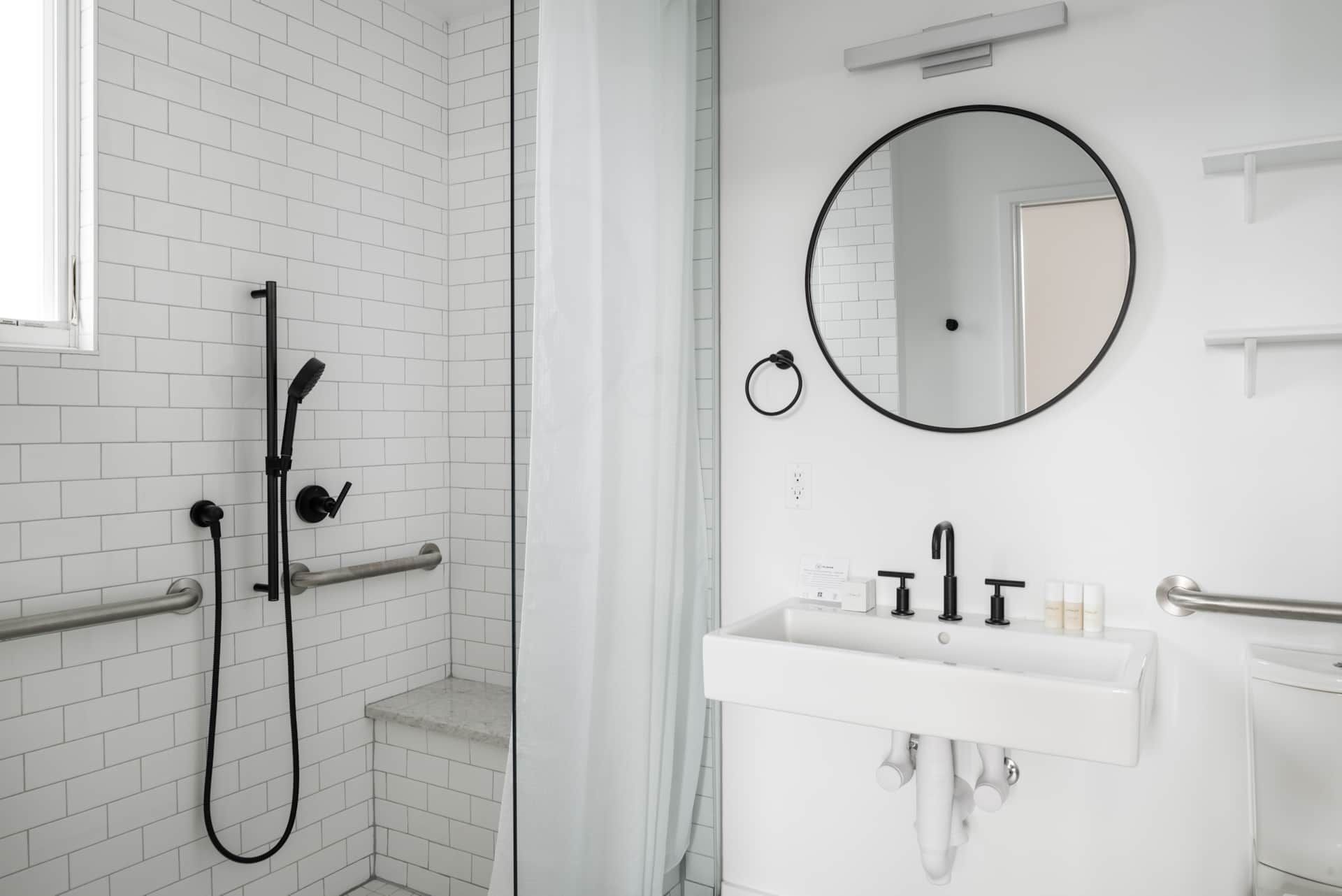 Modern white bathroom with walk-in shower, round mirror, and wall-mounted sink
