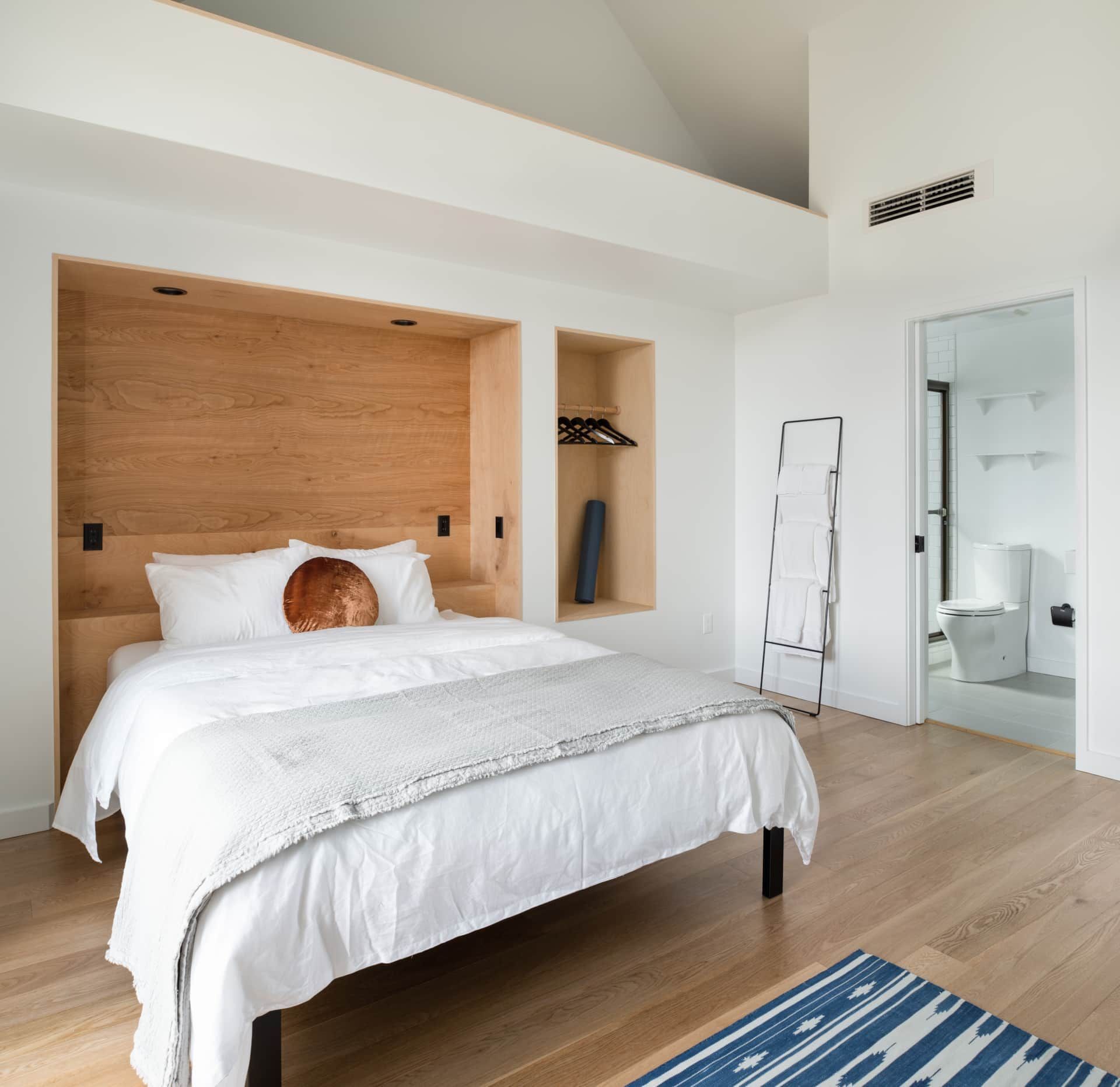 Modern bedroom with white bed, wood accent wall, and mirrored closet.