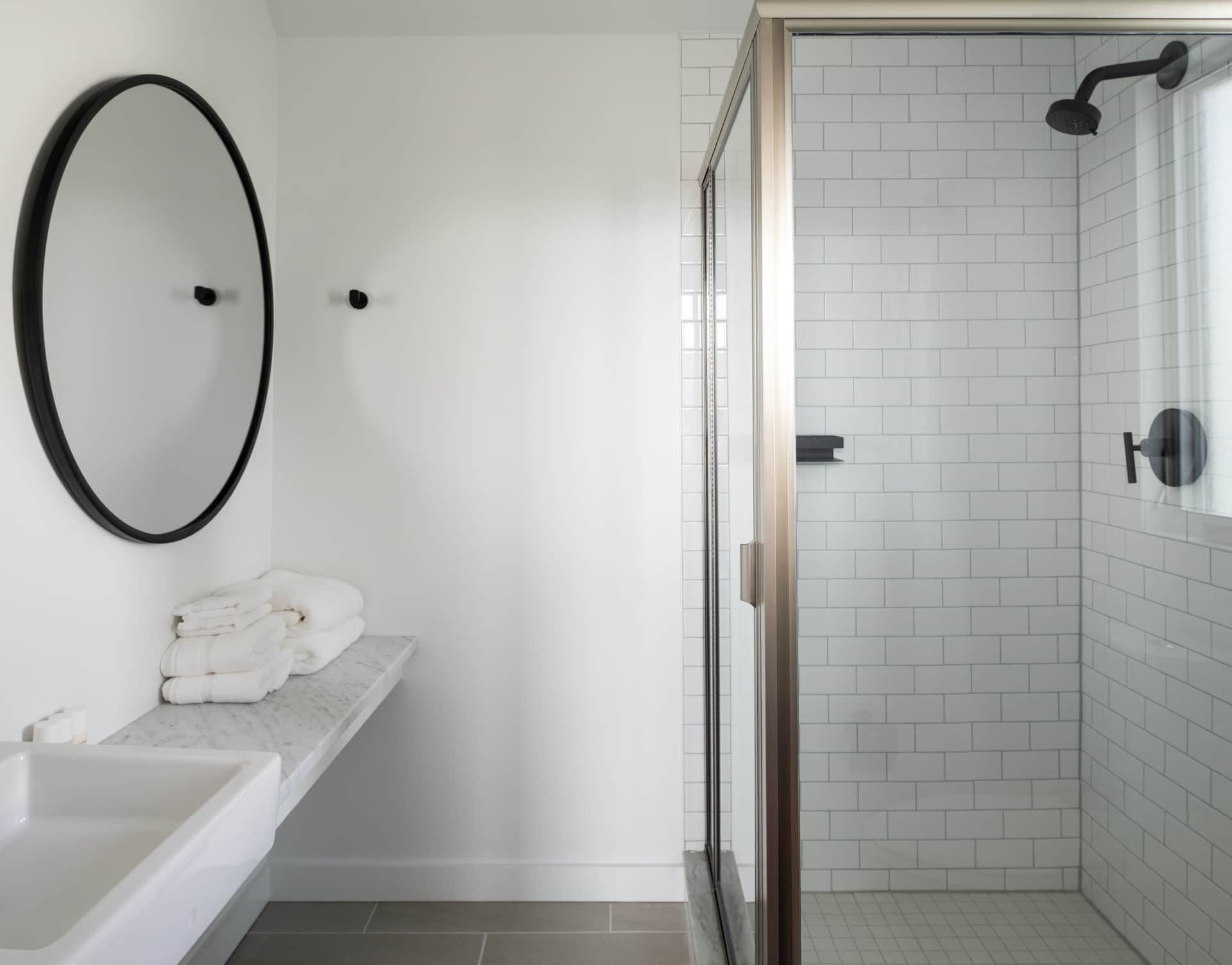 Modern bathroom with round mirror, white vanity, folded towels, and glass shower stall