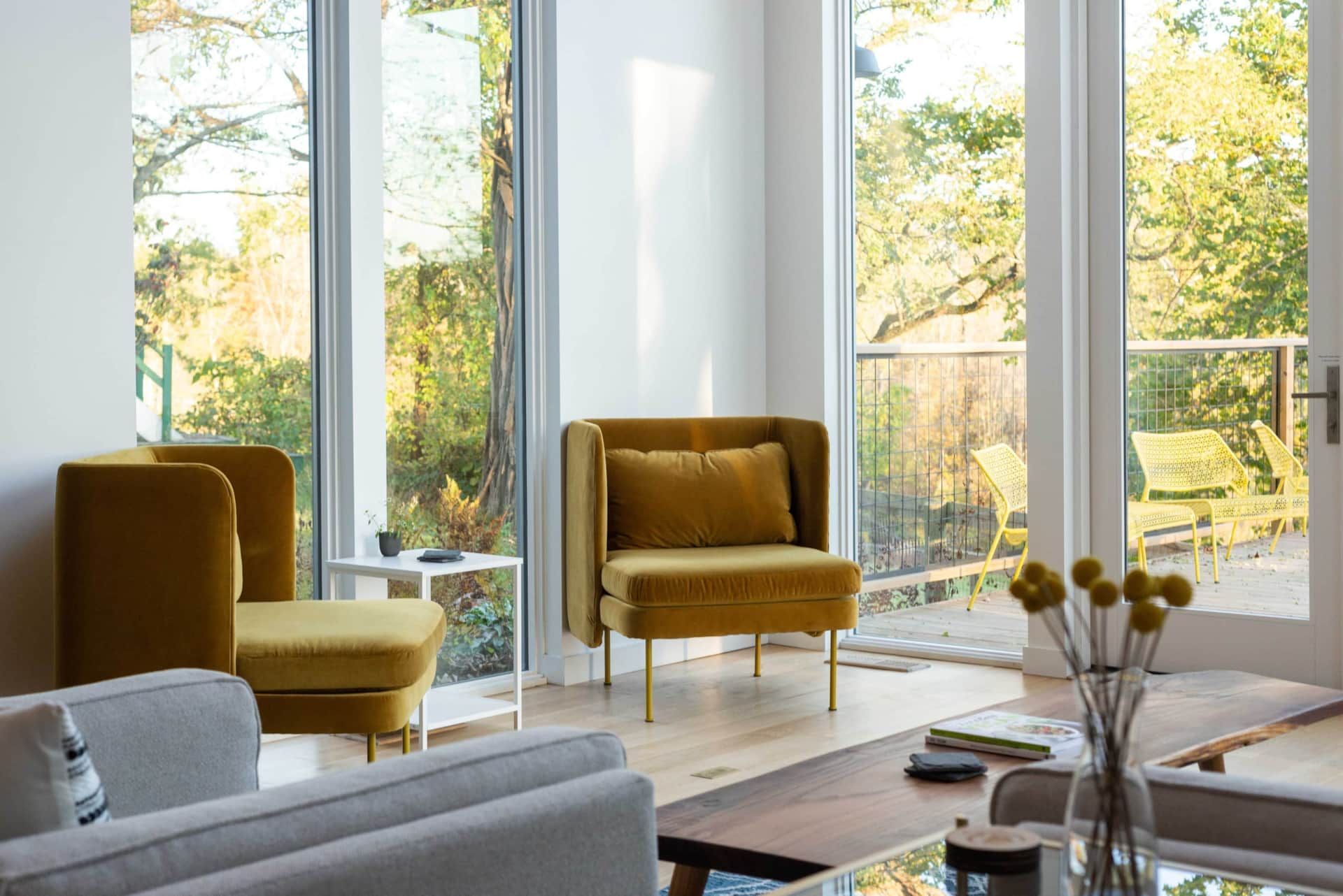 Modern living room with mustard chairs, gray sofa, and large windows overlooking a bright garden