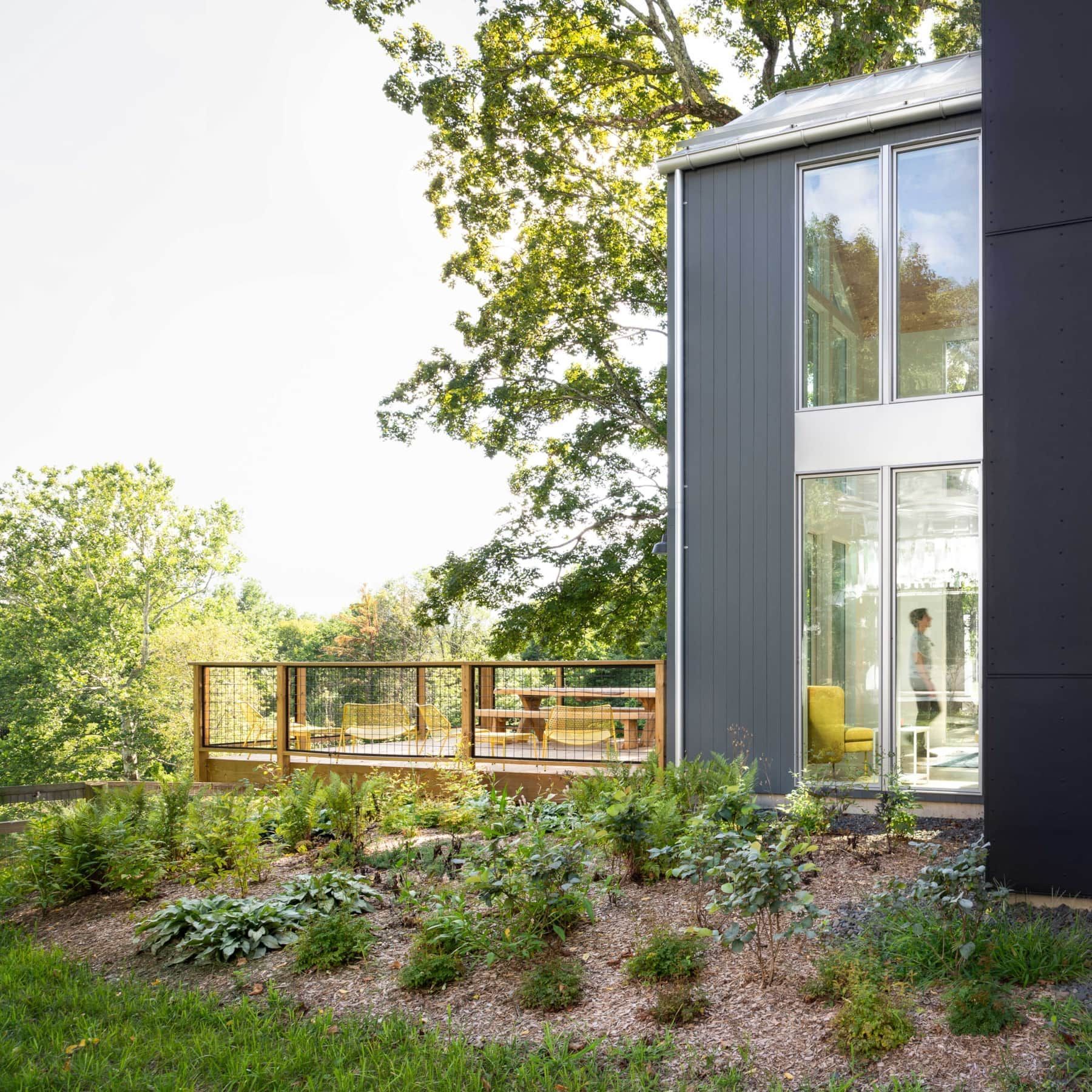 Modern house with tall windows beside a landscaped garden and wooden deck surrounded by trees