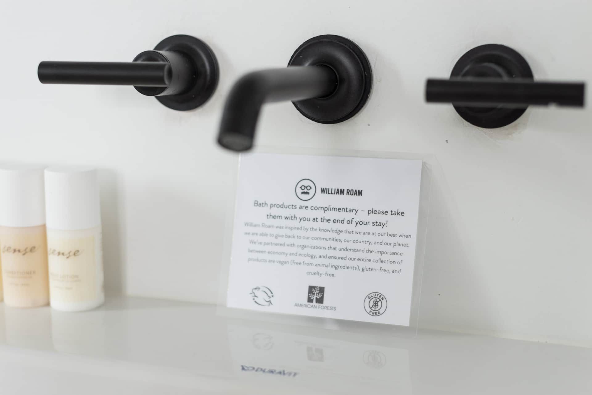Black wall-mounted sink with three matte black faucets above a white countertop and sign.