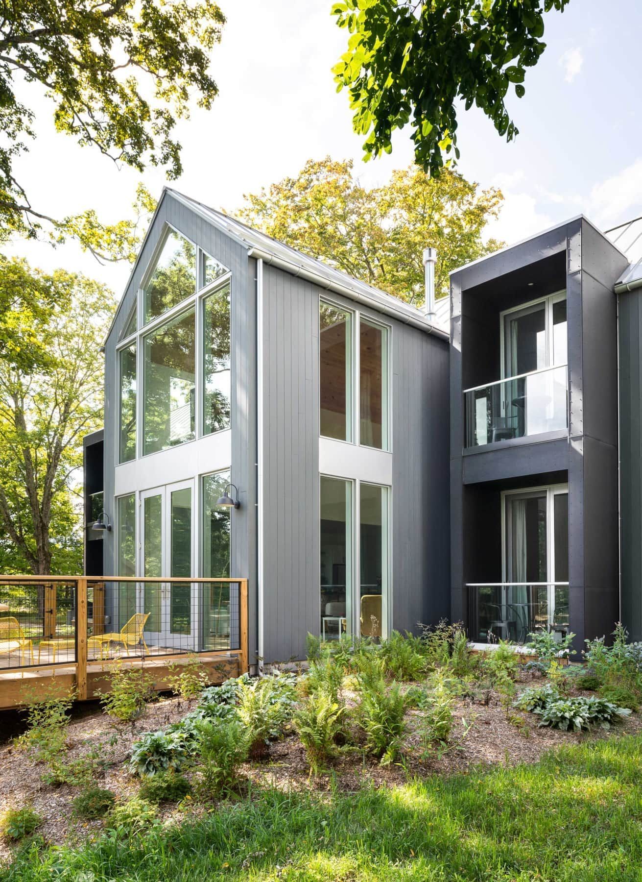 Modern house with tall windows, black and white exterior, and a wooden deck in a leafy garden.