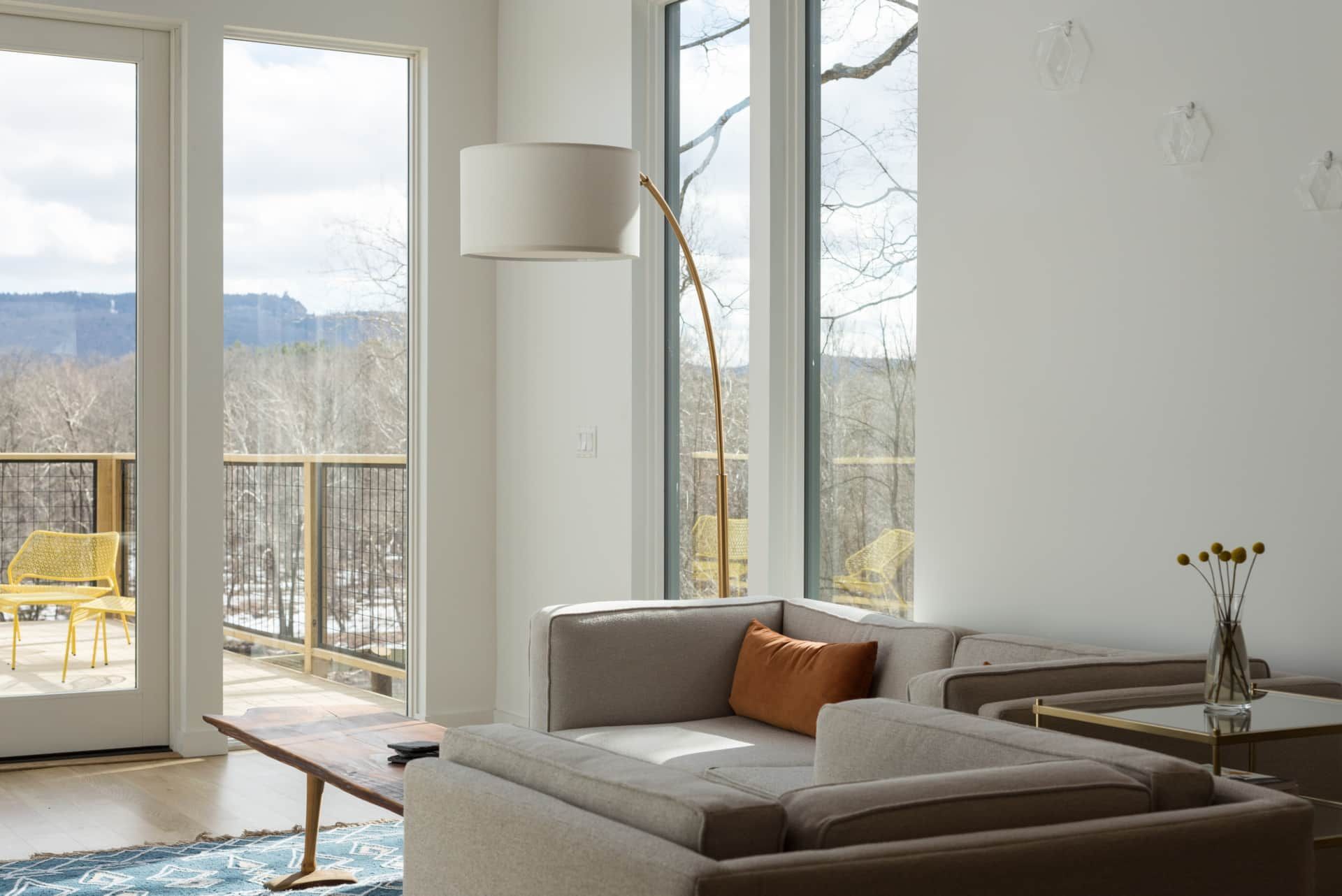 Bright modern living room with large windows, beige sofa, floor lamp, and snowy mountain view outside