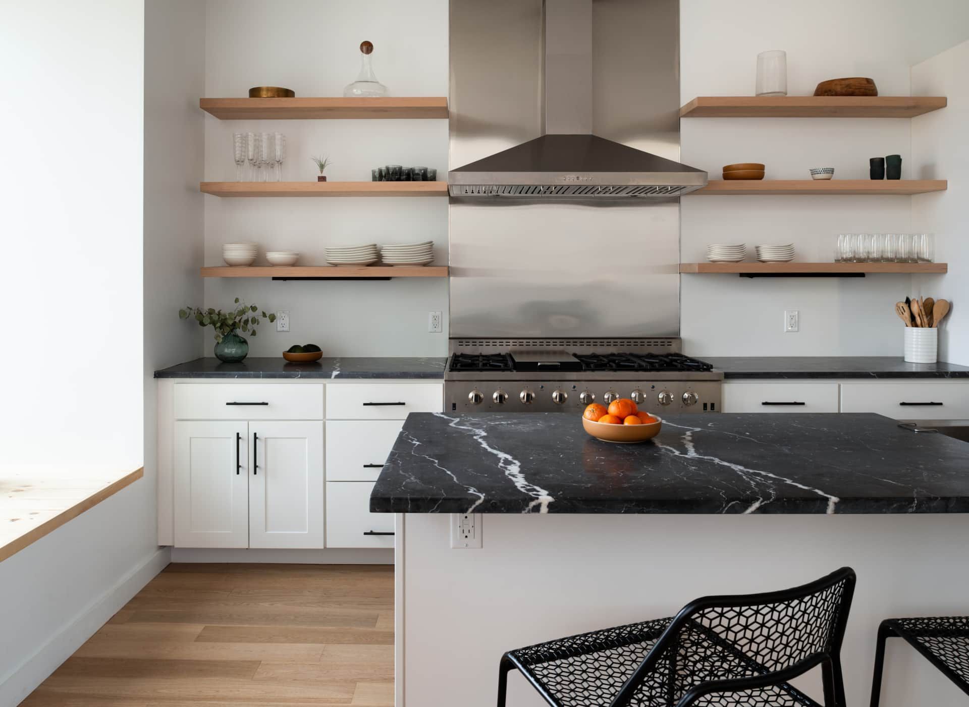 Modern kitchen with white cabinets, open wood shelves, black marble island, and stainless steel range hood