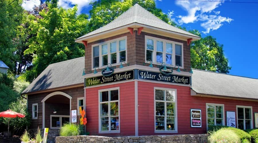 Red historic building with white trim and black signs, surrounded by trees under a blue sky.