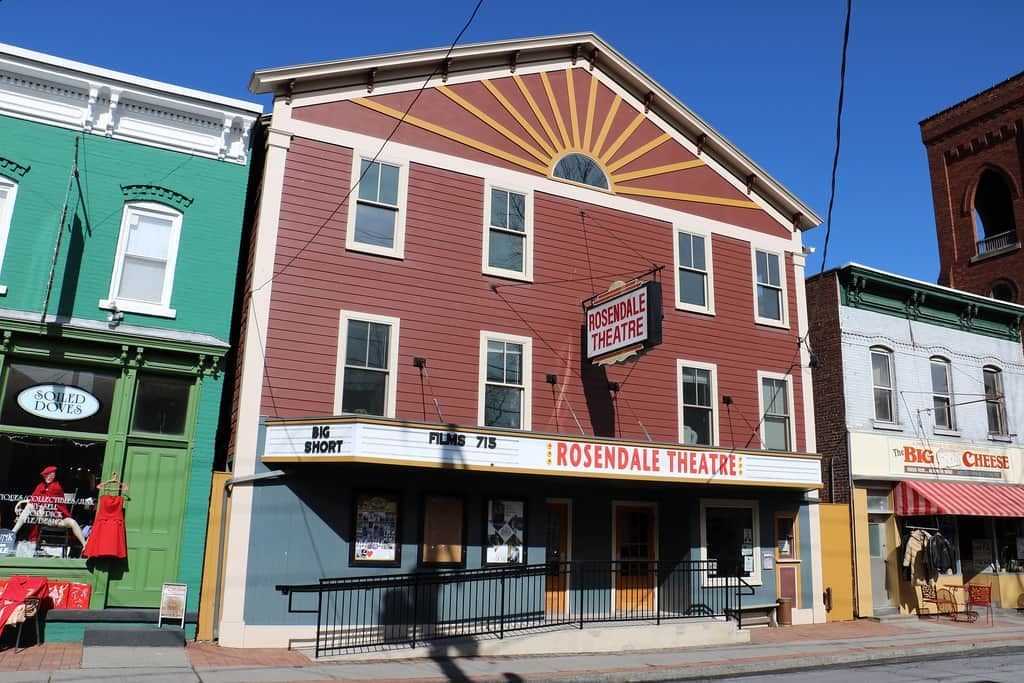 Historic theater facade on a colorful downtown street, with red siding, marquee, and neighboring storefronts.