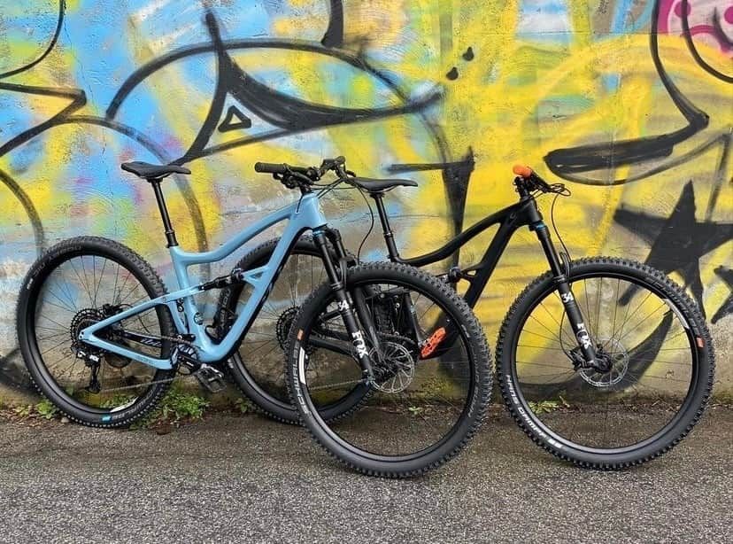 Two mountain bikes, one light blue and one black, parked in front of a colorful graffiti wall.