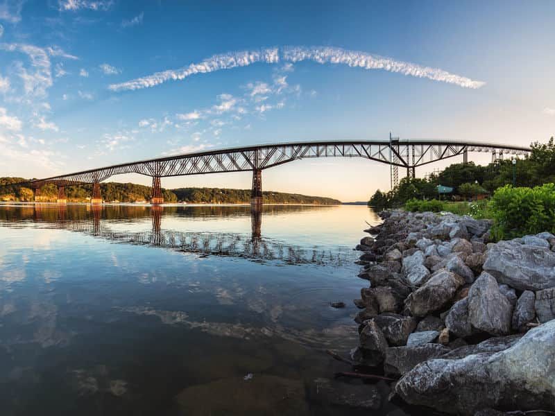 Wide bridge over calm water at sunset, with rocky shoreline and blue sky