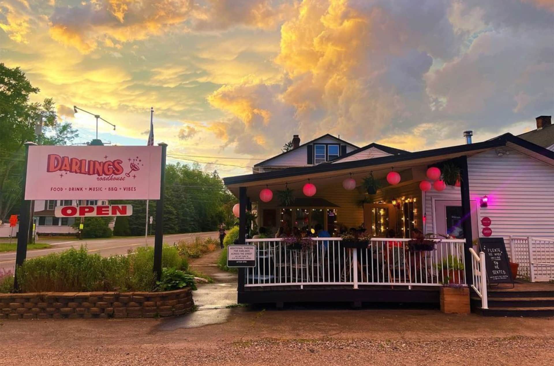 Restaurant with pink lanterns and porch at sunset, with a sign by the roadside.