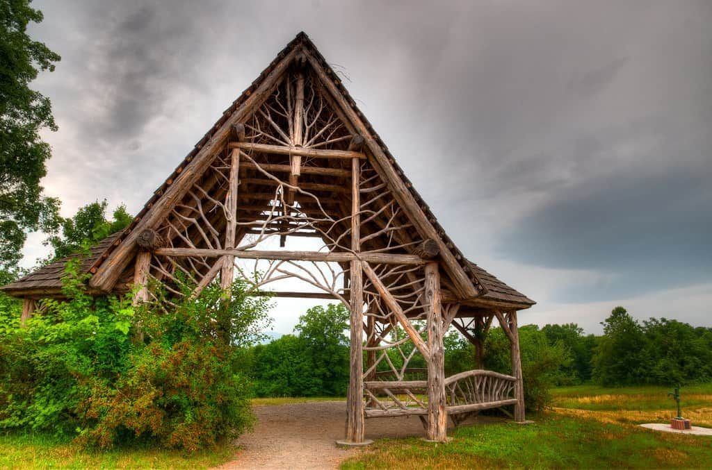 Rustic wooden pavilion with a thatched roof in a green field under a cloudy sky