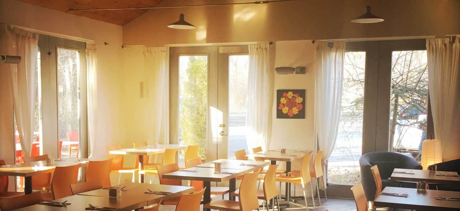 Bright café dining room with wooden tables, hanging lights, and sunlit windows