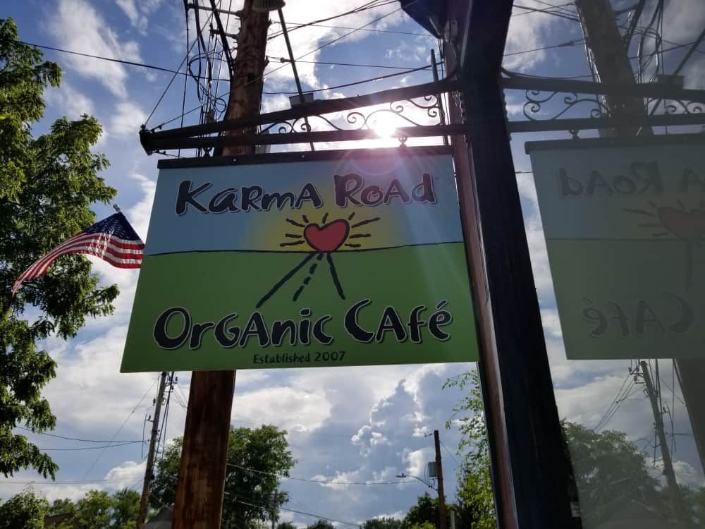 Karma Real Organic Cafe sign under a sunny sky, with an American flag and wooden poles