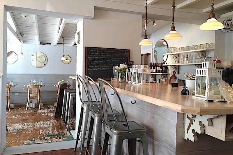 Cozy cafe interior with wooden bar, stools, hanging lights, and tables in a bright rustic space