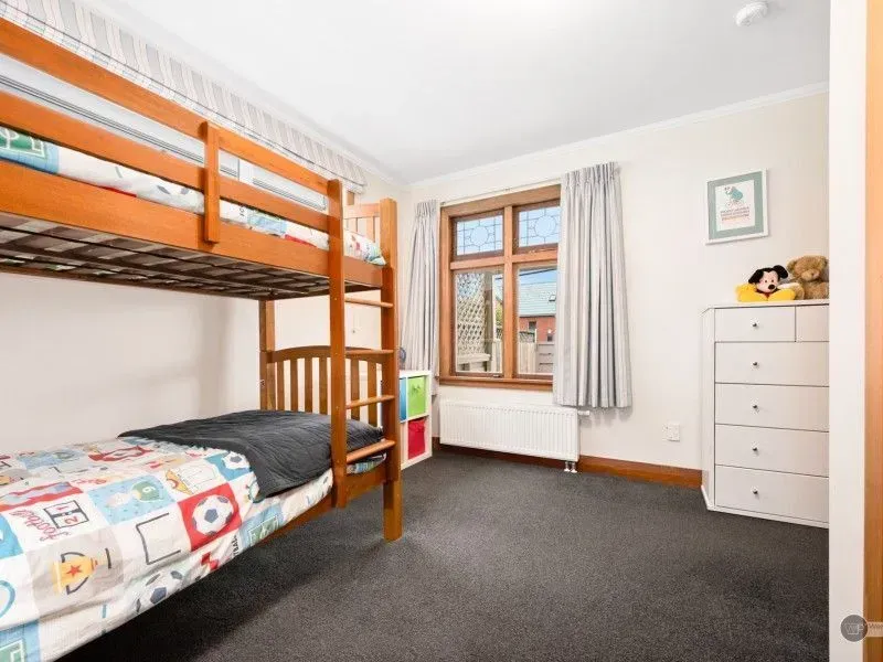 Small bedroom with wooden bunk bed, dresser, window, and gray carpet.